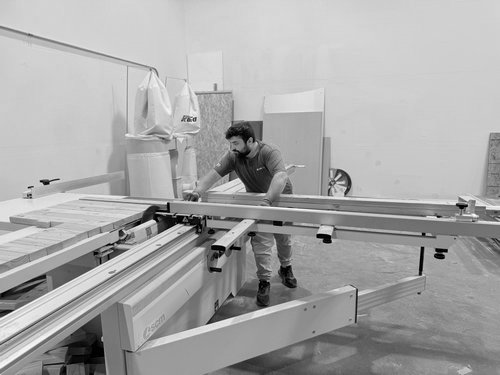 Fabricator sizing a wood panel on a sliding table saw